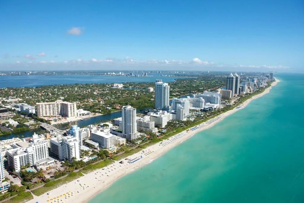 Aerial view of Miami Beach with turquoise water, white sandy shoreline, and modern high-rise hotels along the coast.