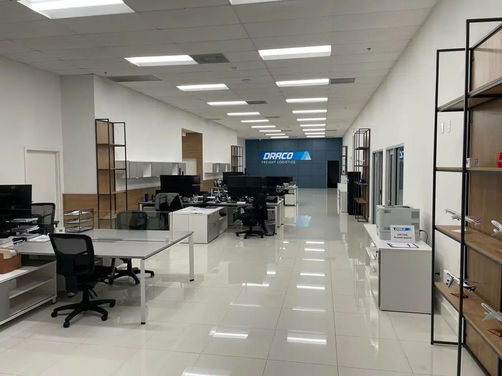 Interior view of Draco Freight Logistics’ modern open office with workstations, minimalist design, and branded wall, reflecting innovation and professionalism in logistics operations.