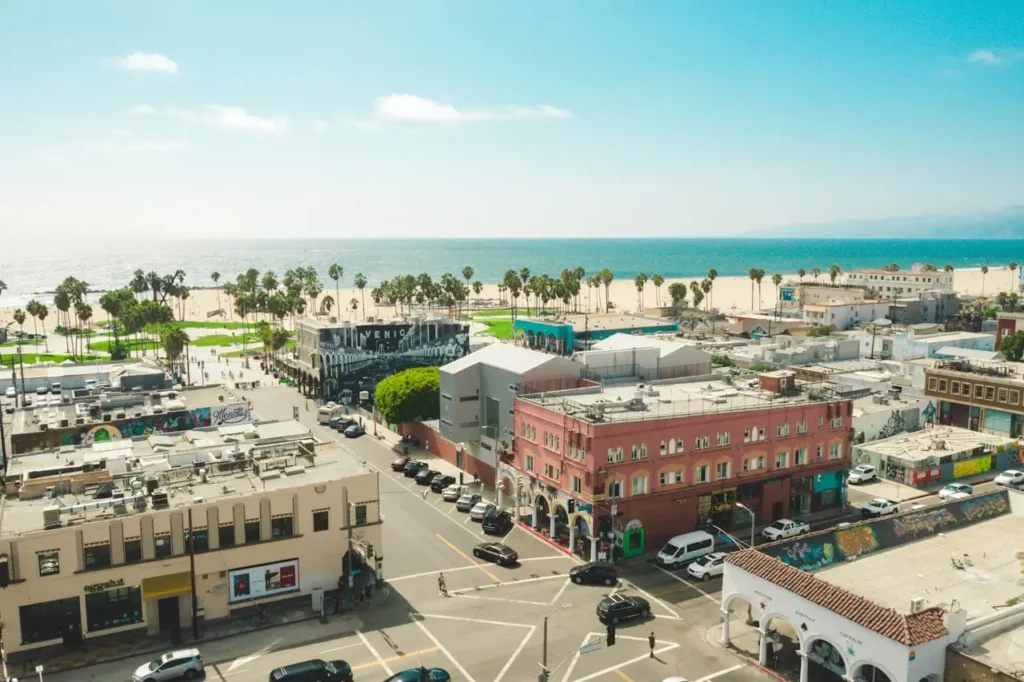 Aerial view of Venice Beach in Los Angeles showing colorful buildings, palm trees, and the sandy beach along the Pacific Ocean.