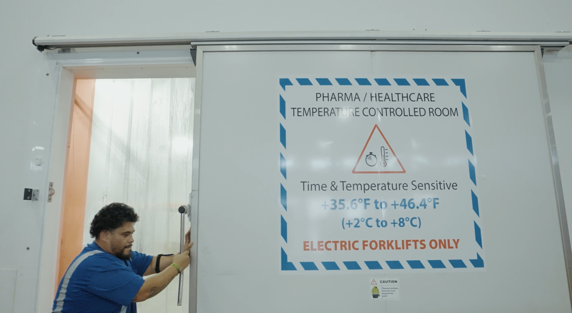 Draco Freight Logistics employee closing temperature-controlled room for pharmaceutical and healthcare cargo in Miami warehouse.